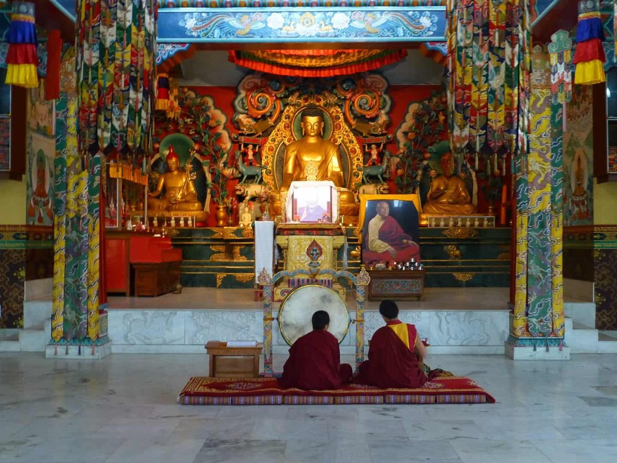 Inside a Tibetan Temple, Bodhgaya, with two people sat before a gold statue of Buddha.