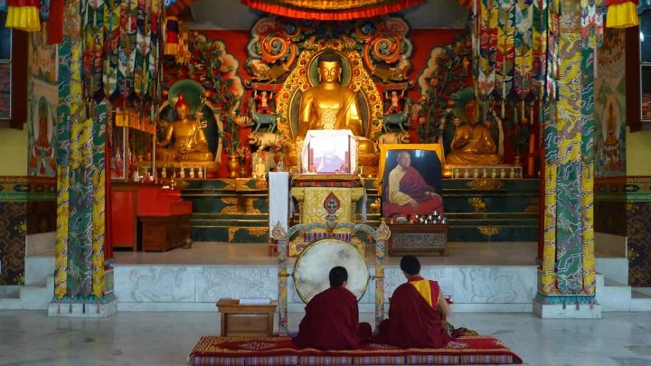 Inside a Tibetan Temple, Bodhgaya, with two people sat before a gold statue of Buddha.