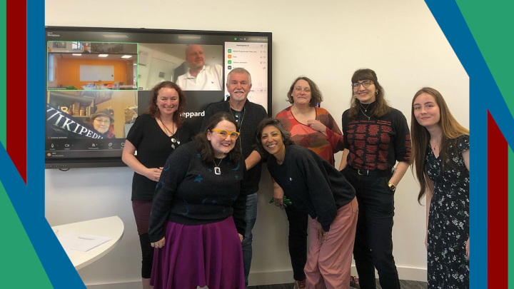 A photo of a smiling group of people in front of a screen showing people who joined the training remotely.