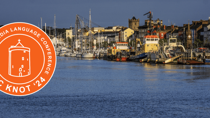 Photograph of boats along a river that runs through the city of Waterford with an orange version of the 2024 Celtic Knot logo